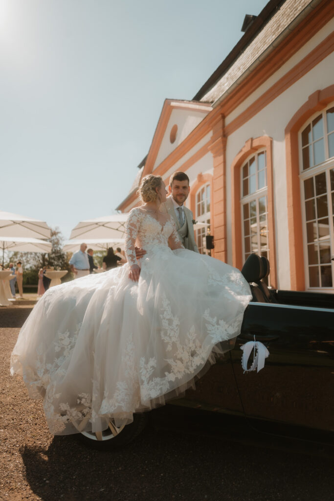 Laura sitzt auf dem Oldtimer vor der Orangerie von Schloss Bekond