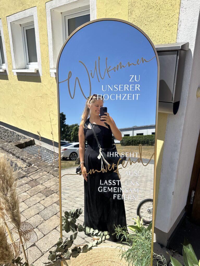 Vicky Diederich mit Kamera bei einer Hochzeit, im Spiegel neben dem Willkommensschild