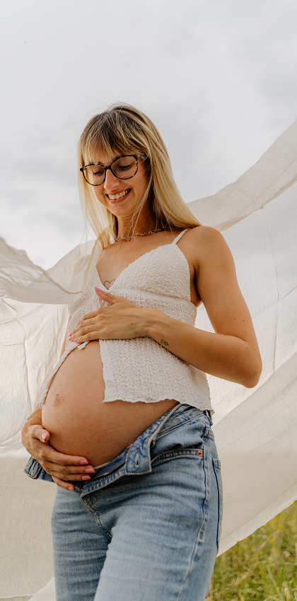 Jana hält ihren Babybauch, hinter ihr weht ein heller Stoff